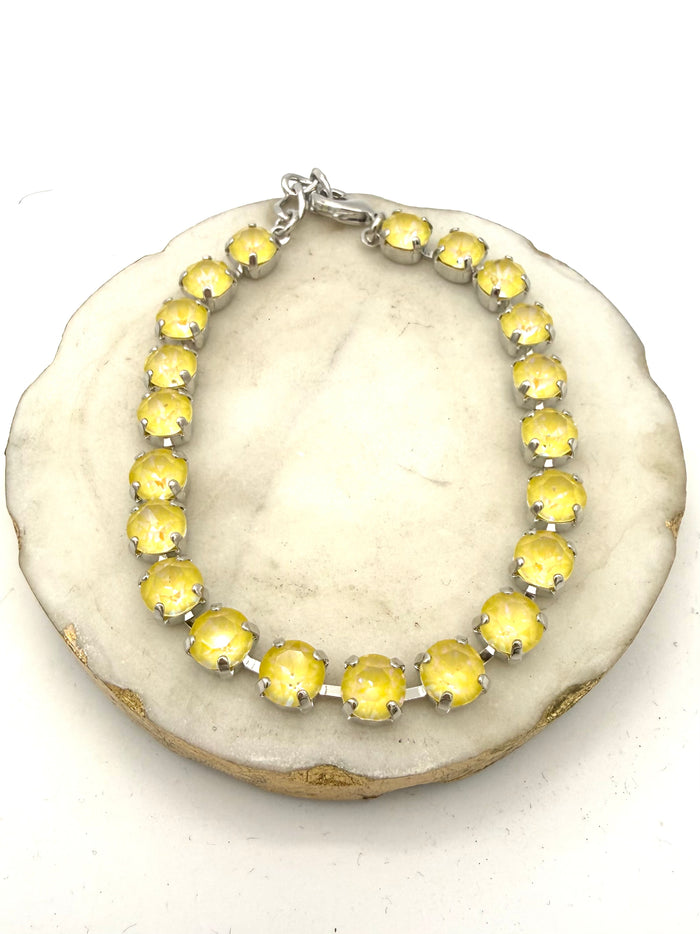 Silver tennis anklet with round milky yellow opalescent stones in prong settings with lobster clasp closure.