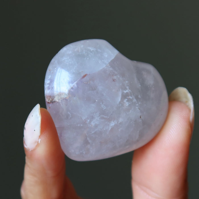 Hand holding a rough-cut amethyst crystal against a dark background