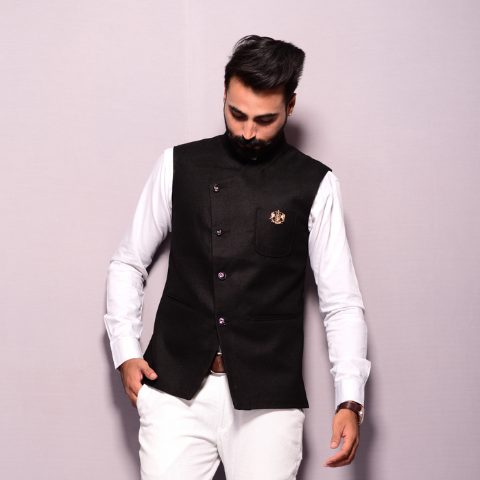 A man wearing a black tweed angrakha style jacket with a mandarin collar and a breast pocket, paired with white trousers.