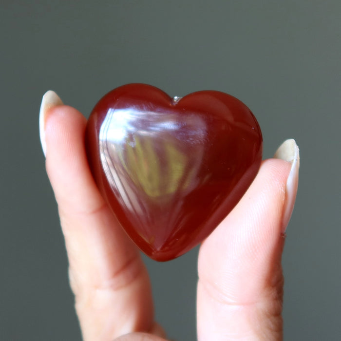 Heart-shaped carnelian held between fingers against a gray background