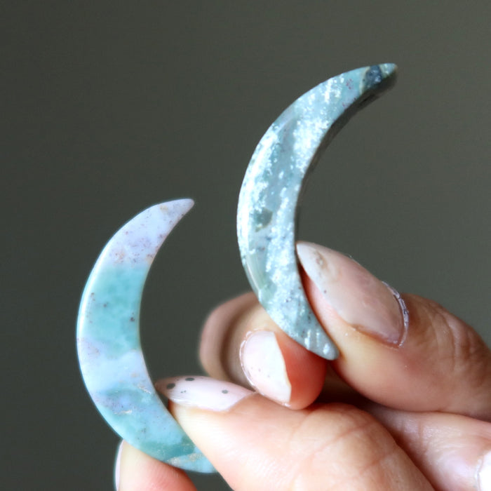 Hand holding two japer stone crescent moon shapes against a dark background