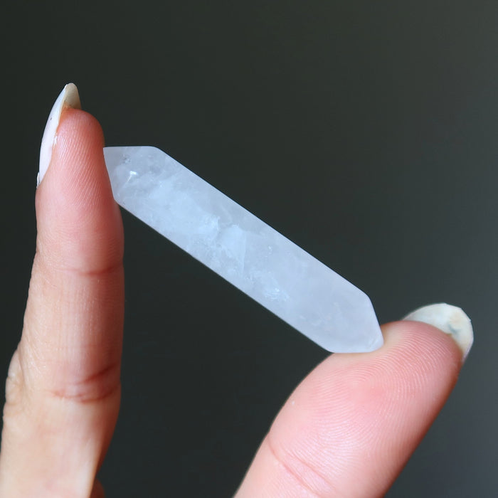 clear quartz doubleterminated crystal held between fingers against a dark background
