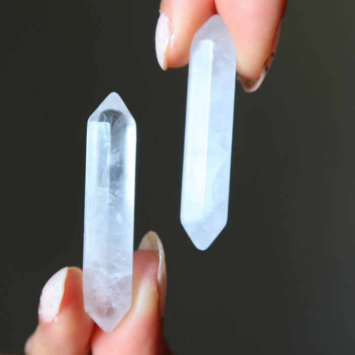 Two clear quartz doubleterminated points held between fingers against a dark background