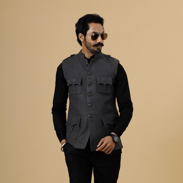 A man wearing a dark grey tweed semi-hunting Rajputana jacket with pockets on the chest, paired with black trousers and sunglasses.