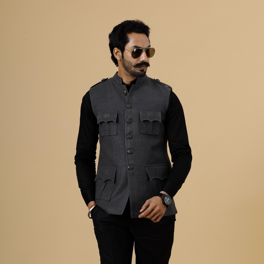 A man wearing a dark grey tweed semi-hunting Rajputana jacket with pockets on the chest, paired with black trousers and sunglasses.