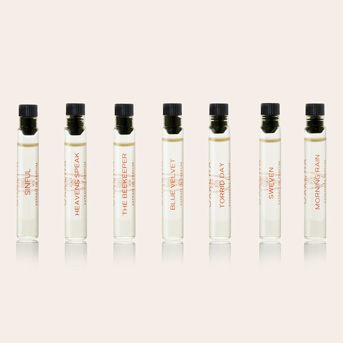 Front view of seven perfume oil sample vials showcasing clear glass tubes with black caps on a pale pink background