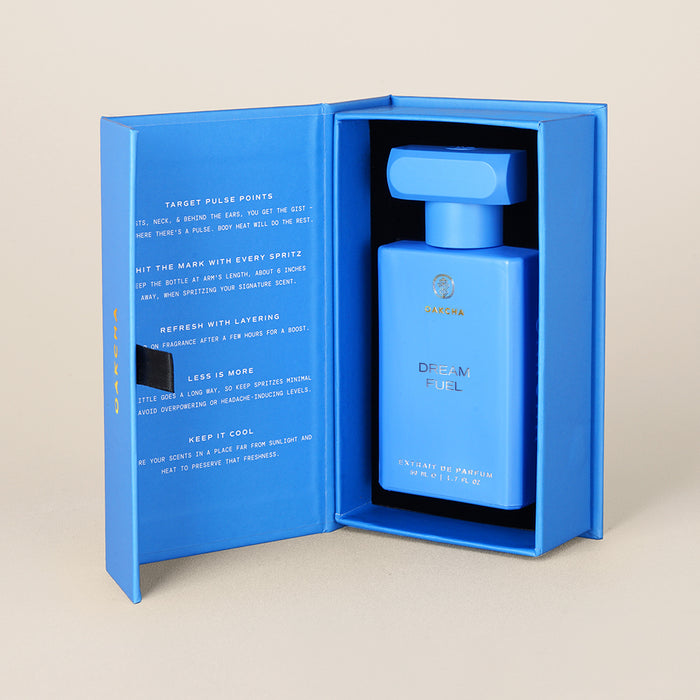 Front view of 50 ml Dream Fuel perfume bottle inside open blue presentation box on beige background