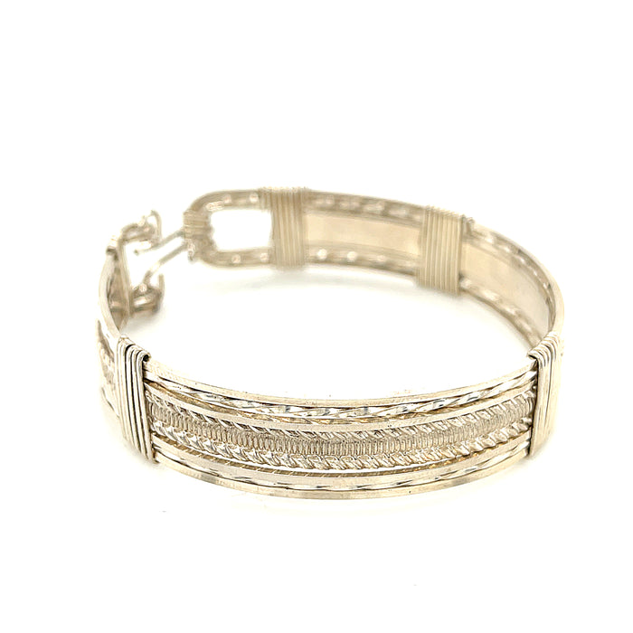 Handcrafted sterling silver wire-wrapped bangle with twisted and straight wire combination showing polished dome centerpiece, on a white background, front right angle view.