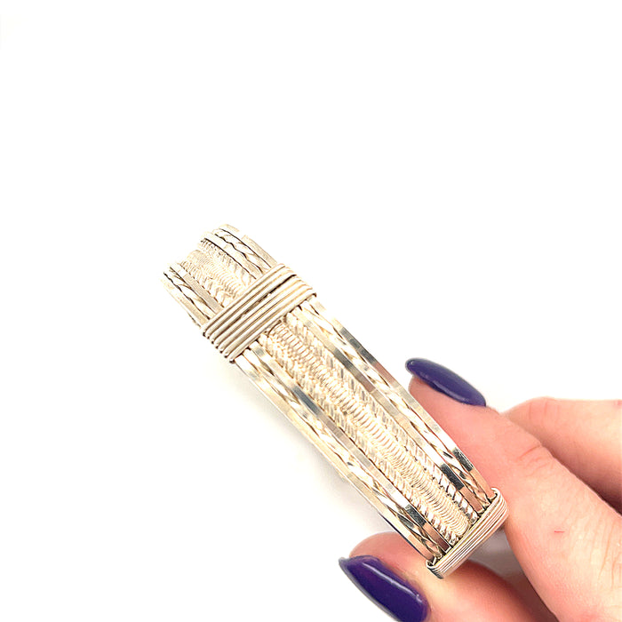 Style #1 Handcrafted sterling silver wire-wrapped bangle with twisted and straight wire combination showing polished dome centerpiece, on a white background in the model's hand, front view.