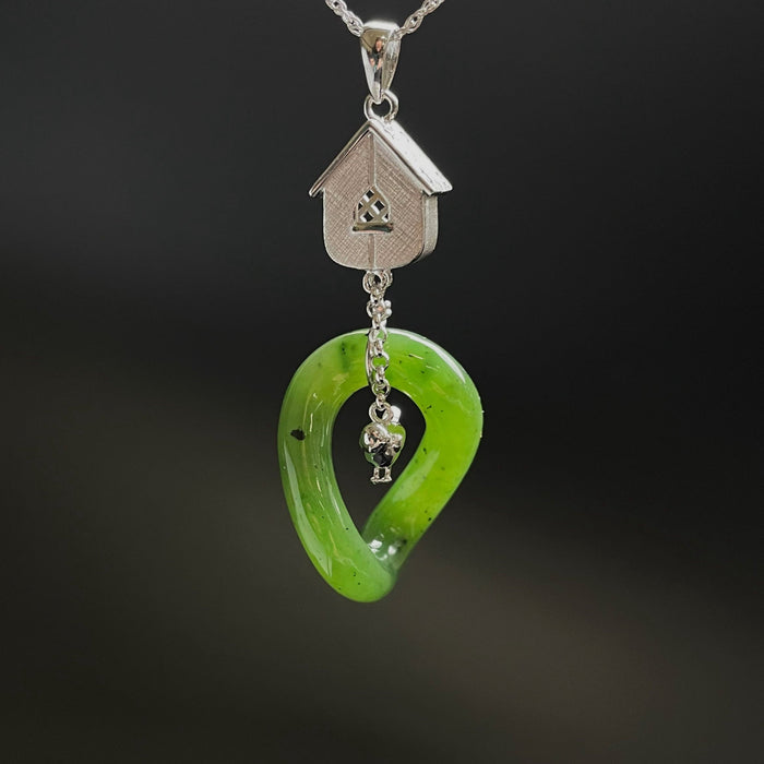 Green jade pendant with silver house and heart design on a dark background