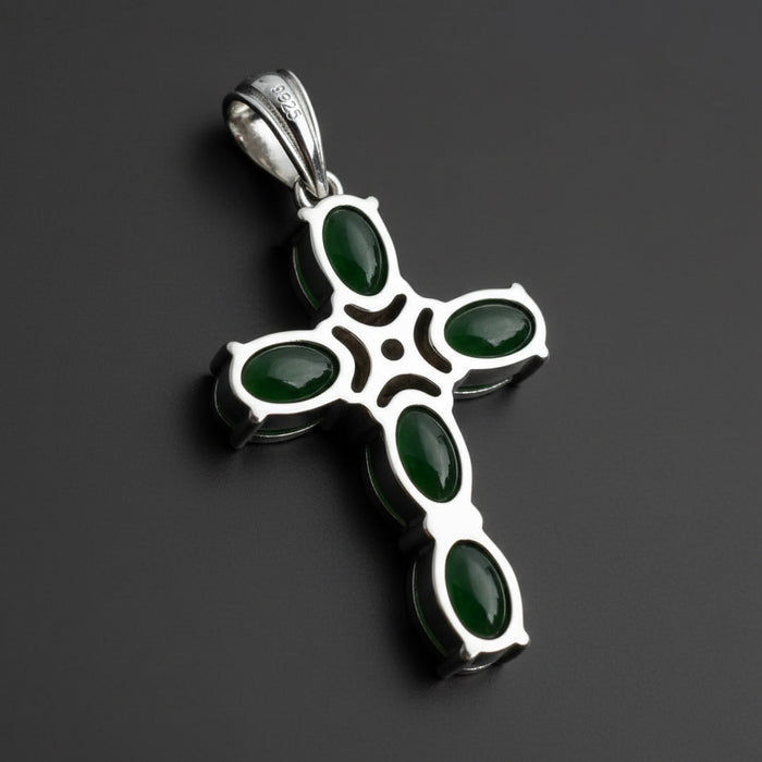Silver cross pendant with green stones on a wooden surface