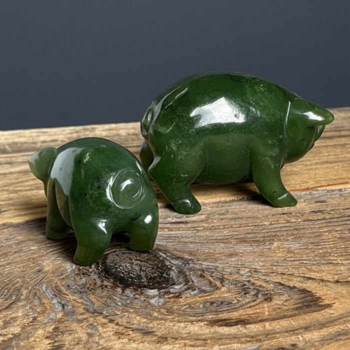 Two green jade pig figurines on a wooden surface with a neutral background