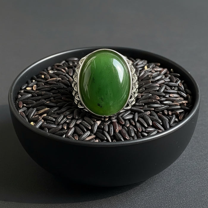 Green jade stone ring with silver band on a wooden surface