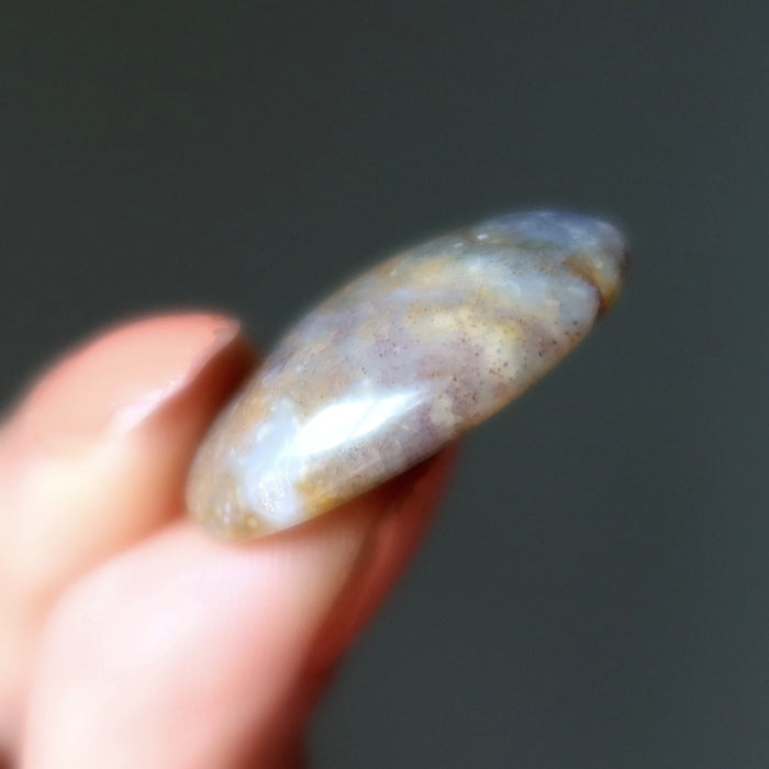 Hand holding a smooth, oval-shaped stone against a dark background
