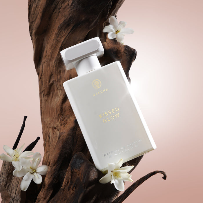 Front view of Kissed Glow perfume bottle showcasing white frosted rectangular bottle with gold logo and cap on wood background