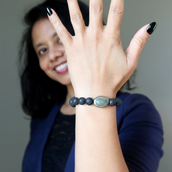 Woman wearing a lava and pyrite beaded bracelet on her wrist with a gray background