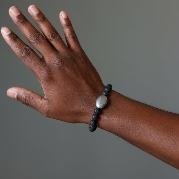 Hand wearing a dark lava beaded bracelet with a pyrite charm on a gray background