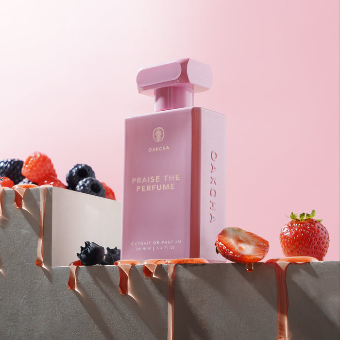 Three-quarter view of Praise the Perfume 100 mL bottle with berries and chocolate on a pink background