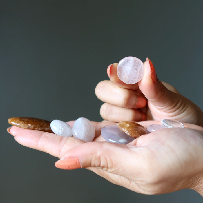 Hands holding various stones against a dark background