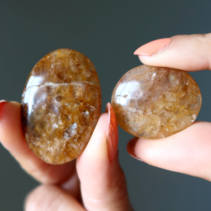 Two brown stones held between fingers against a dark background
