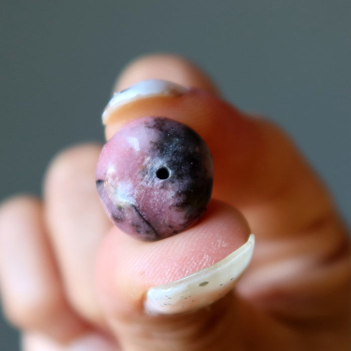 Hand holding a Rhodonite apple stone against a neutral background