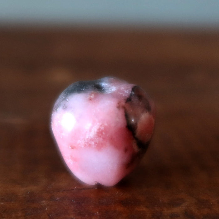 Small pinkish Rhodonite apple stone on a wooden surface