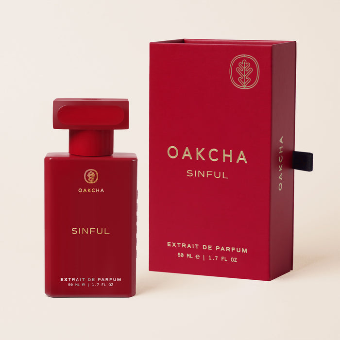 Front view of Sinful Extrait de Parfum bottle and box showcasing red packaging and 50 ml size on beige background