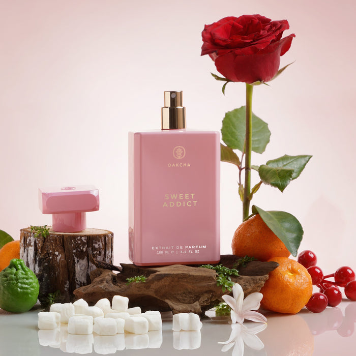 Front view of Sweet Addict perfume bottle, 100 mL, with pink bottle, gold spray, red rose, citrus fruit and marshmallows