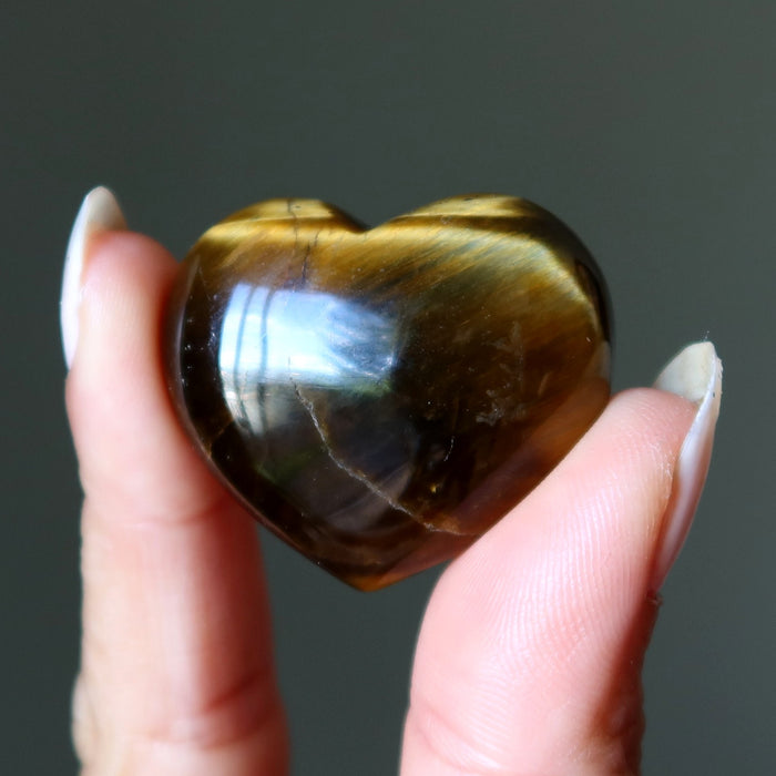 Heart-shaped tiger's eye stone held between fingers against a dark background